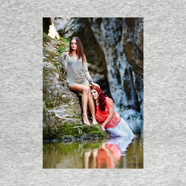 Two beautiful young women leaning on rocks beside a river by naturalis